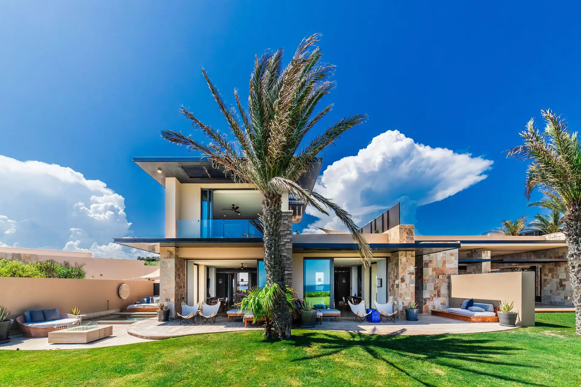 The residence's three separate lock-off wings, each with its own private lounge and terrace, arranged around a central palm-shaded lawn.