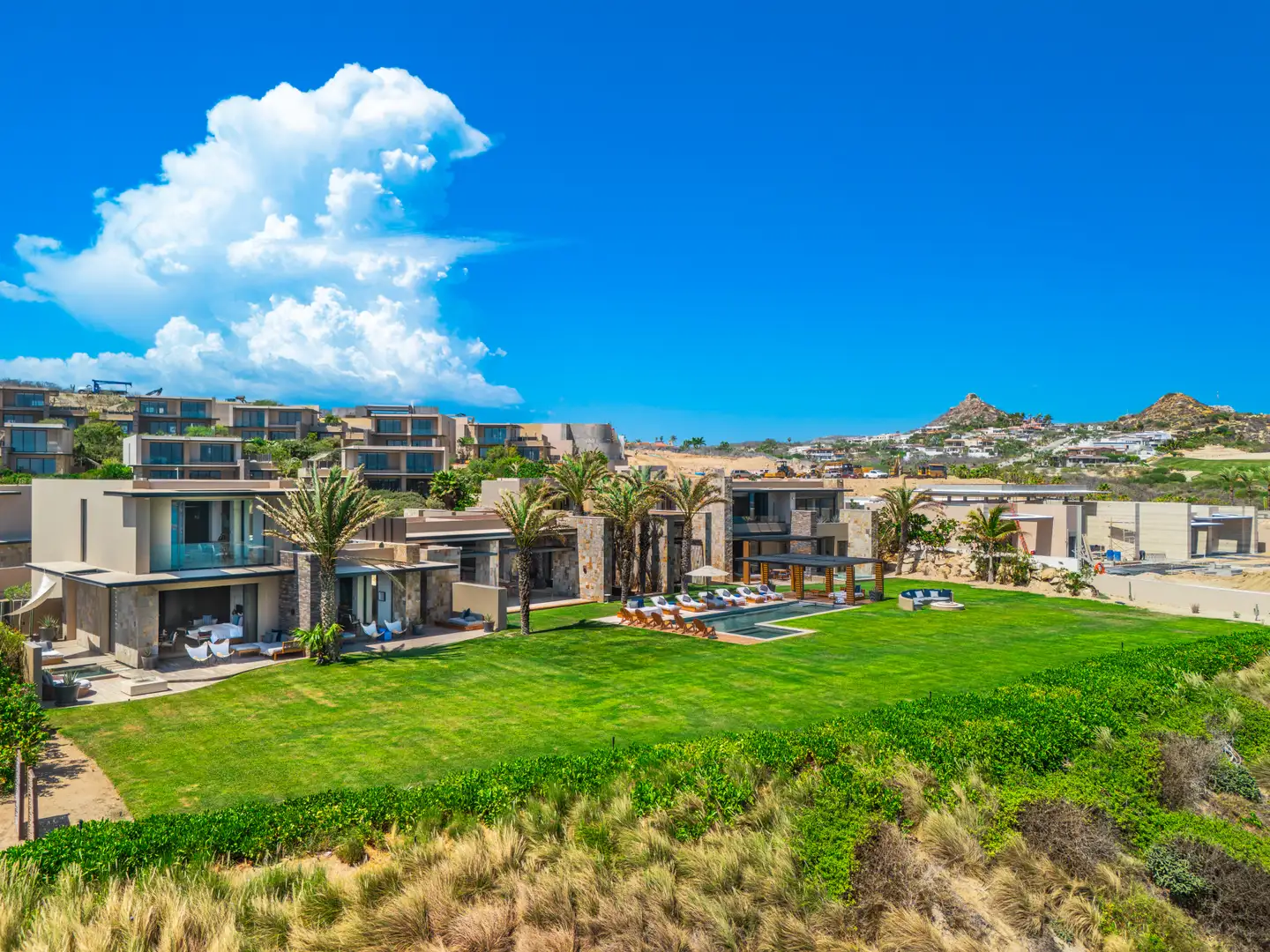 Aerial establishing view of a cluster of Grand Reserve residences and their shared lawn, pool terrace in the foreground, ocean beyond.