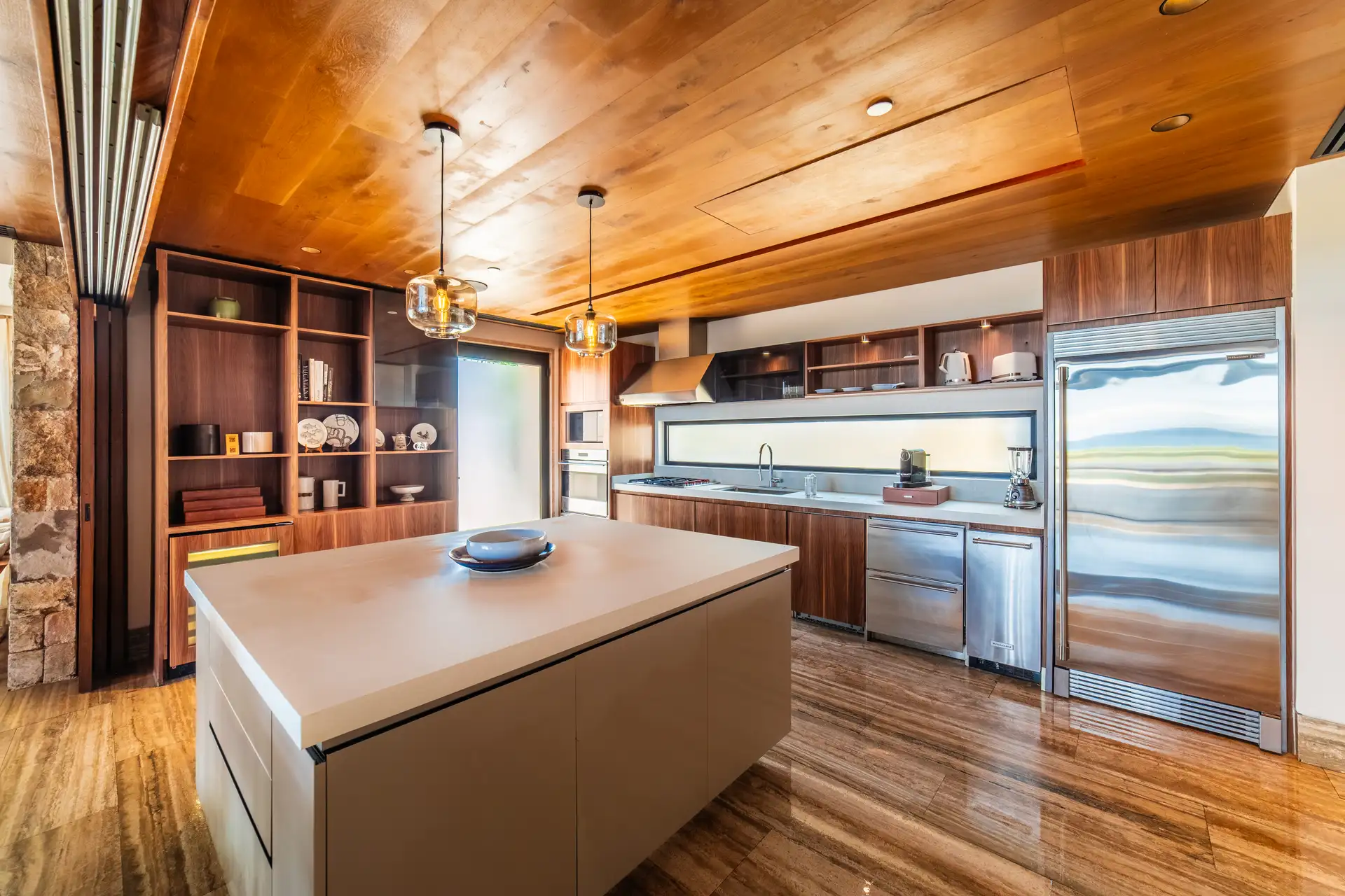 Chef's kitchen with a long waterfall-edge island, pendant lighting, and integrated stainless appliances, opening onto the dining and living areas.