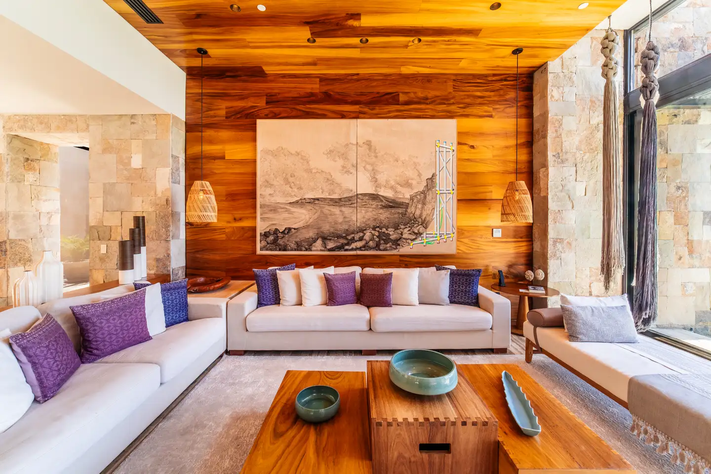 Living room interior with a wood-paneled accent wall, framed artwork, and cream sofas accented with purple and white pillows