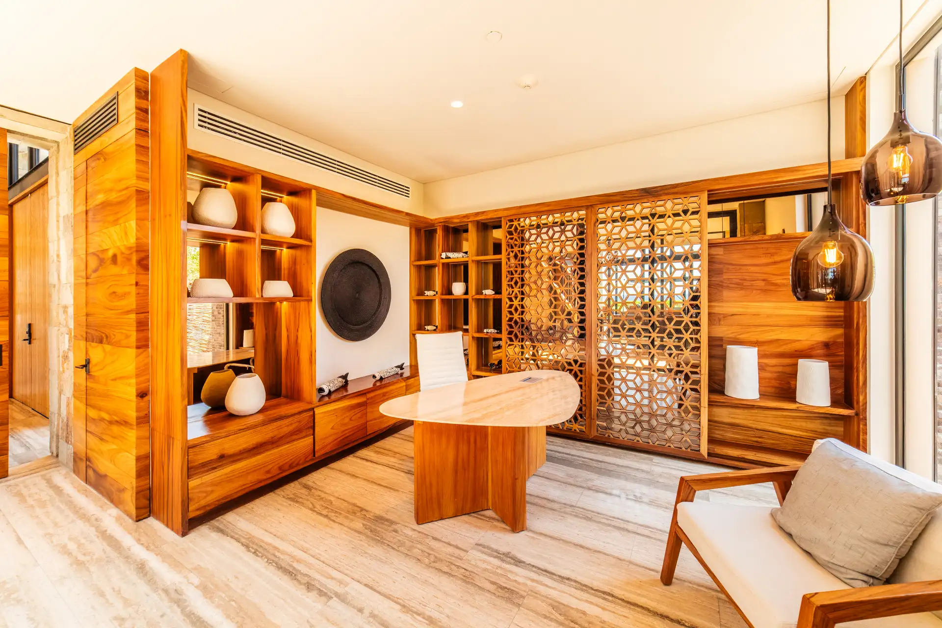 A private sitting room within the residence, with floor-to-ceiling walnut built-in shelving, a round wood table, a carved fretwork screen, and woven pendant lighting.