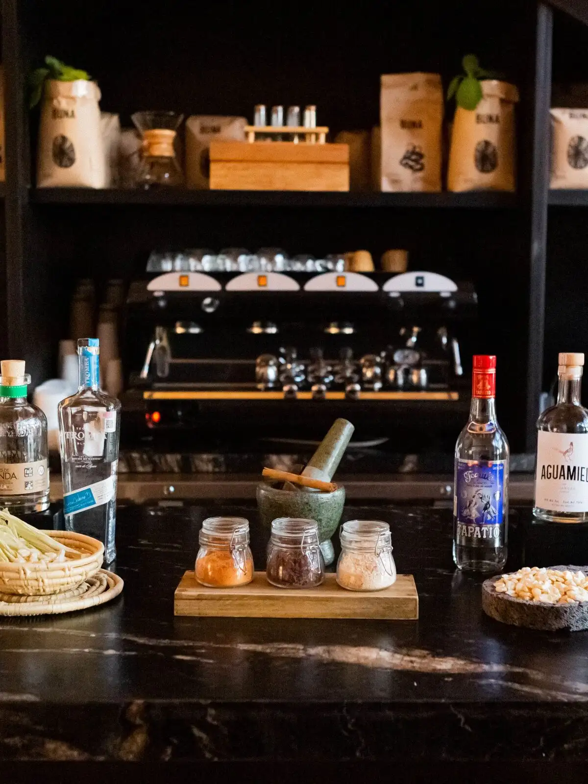 Candil's dark agave-bar counter and back-bar, lined with bottles of tequila and mezcal, a stone mortar and pestle, and a brick archway behind the espresso station.